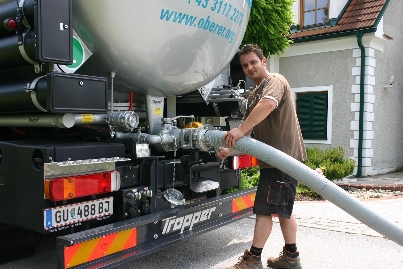 Mann bedient Tankfahrzeug mit Schlauch vor Haus, Pelletslieferung in Arbeit.