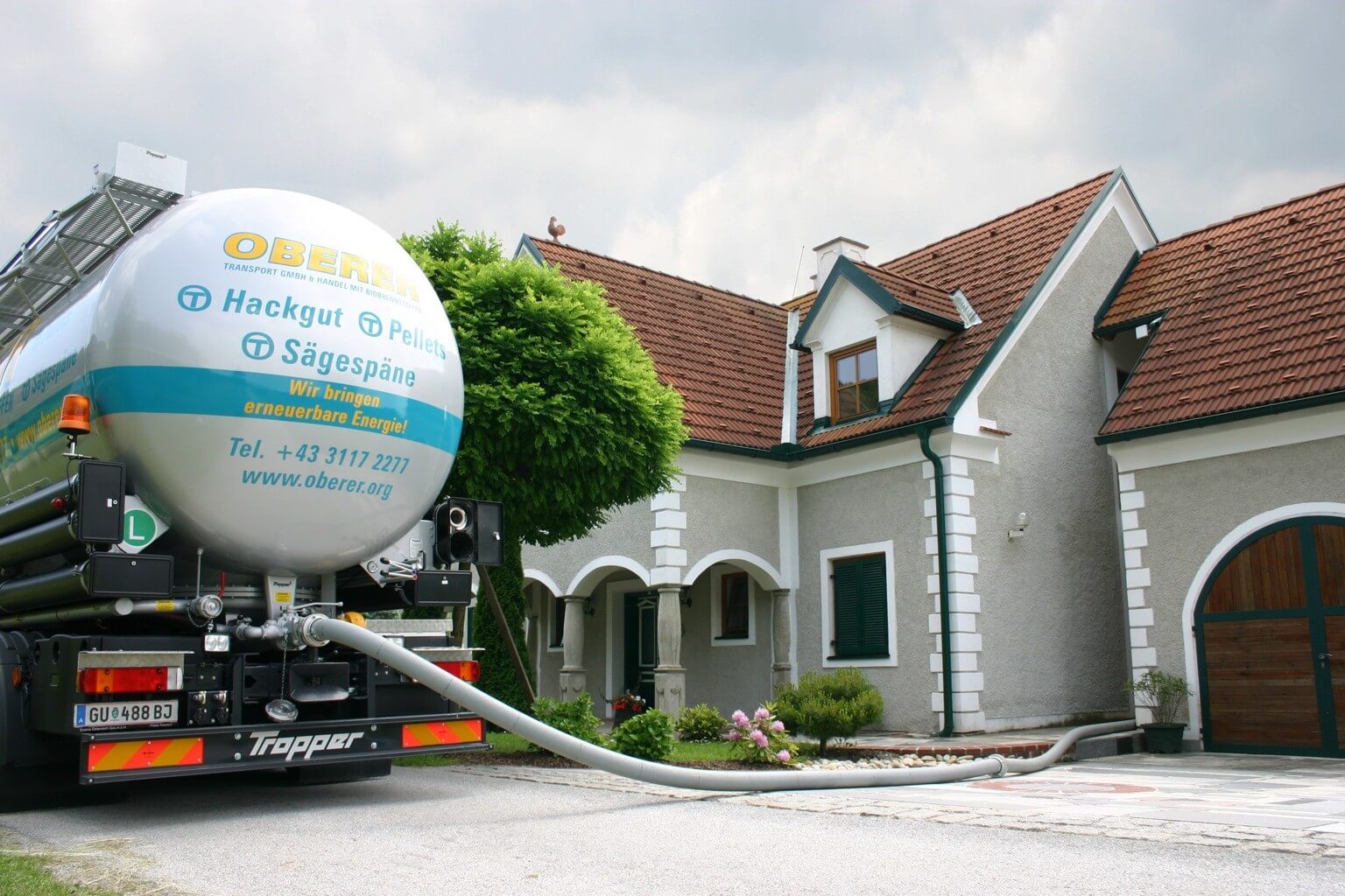 LKW liefert erneuerbare Energien an ein Haus: Hackgut, Pellets, Sägespäne. Nachhaltige Energieversorgung vor Ort.