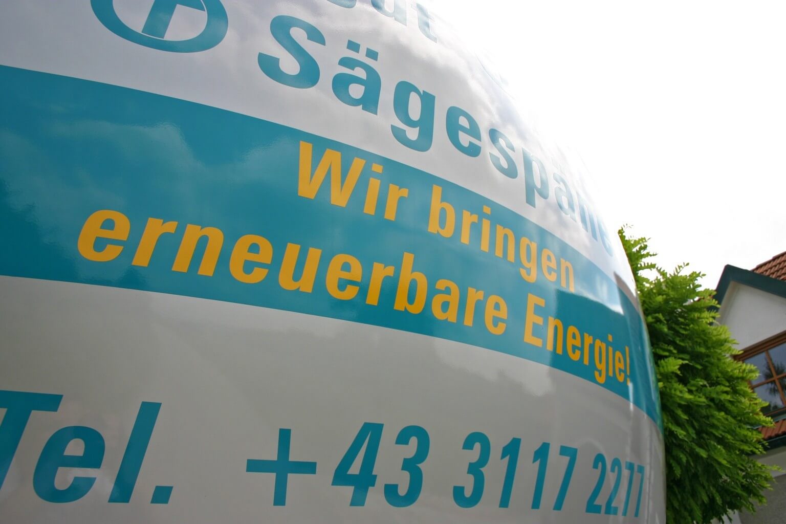 Slogan auf Fahrzeug: Wir bringen erneuerbare Energie!“ vor einem Gebäude mit grünen Bäumen im Hintergrund.